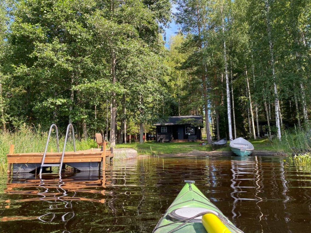 Kuva kanootista tulossa rantaan. Rannalla mökki.