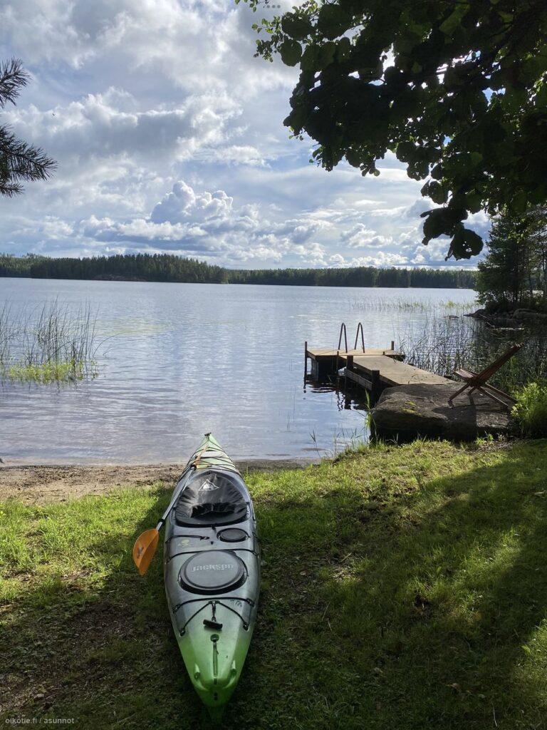 Kanootti nurmikolla rannassa. Taustalla järvi ja vastarannan metsä.